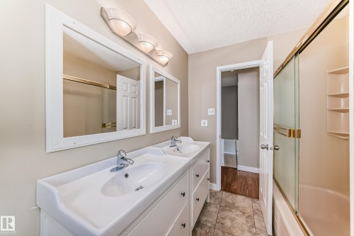 Bathroom with double vanity, bath / shower combo with glass door, and a textured ceiling - 38 Lancaster Crescent, St. Albert, AB - Indoor Photo Showing Bathroom