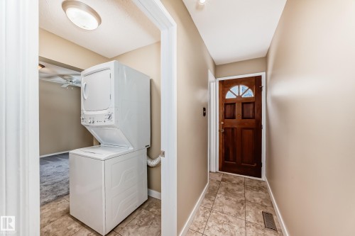 Laundry room featuring stacked washer / drying machine and light tile patterned floors - 38 Lancaster Crescent, St. Albert, AB - Indoor Photo Showing Laundry Room