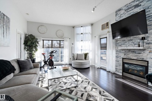 Living area with dark wood-type flooring, a fireplace, and a textured ceiling - 302 10905 109 Street, Edmonton, AB - Indoor Photo Showing Living Room With Fireplace