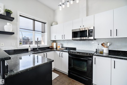 Recently renovated kitchen with black electric range, dark stone counters, stainless steel microwave, white cabinets, and open shelves - 302 10905 109 Street, Edmonton, AB - Indoor Photo Showing Kitchen With Double Sink
