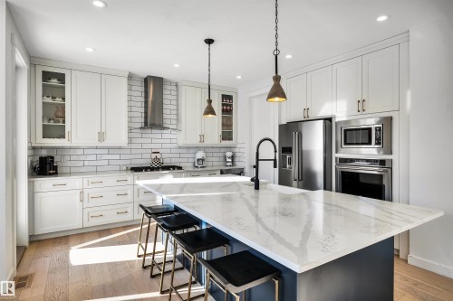 Kitchen with glass fronted cabinets, a kitchen breakfast bar, light stone counters, a center island with sink, and light wood finished floors - 11 Promenade Point(E), Beaumont, AB - Indoor Photo Showing Kitchen With Upgraded Kitchen