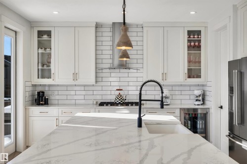 Kitchen featuring glass fronted cabinets, pendant lighting, white cabinetry, light stone counters, and wine cooler - 11 Promenade Point(E), Beaumont, AB - Indoor Photo Showing Kitchen With Upgraded Kitchen
