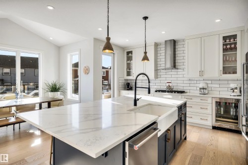 Kitchen with glass insert cabinets, light stone countertops, two tone color scheme, light wood finished floors, and beverage cooler - 11 Promenade Point(E), Beaumont, AB - Indoor Photo Showing Kitchen With Upgraded Kitchen