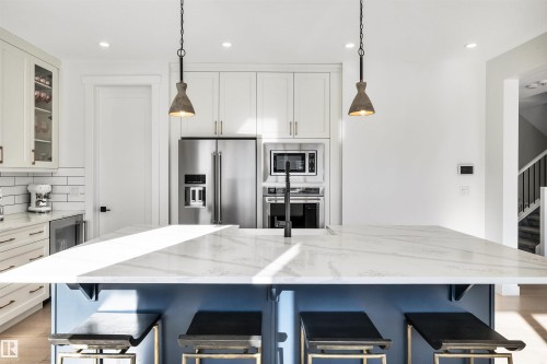 Two tone kitchen with light stone countertops, hanging light fixtures, stainless steel appliances, glass insert cabinets, and dual tone cabinets - 11 Promenade Point(E), Beaumont, AB - Indoor Photo Showing Kitchen With Upgraded Kitchen