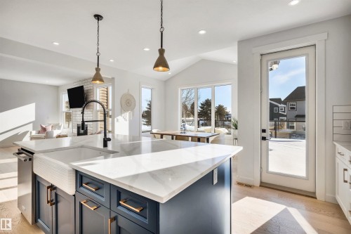 Kitchen with decorative light fixtures, light stone counters, a kitchen island with sink, open floor plan, and blue cabinets - 11 Promenade Point(E), Beaumont, AB - Indoor Photo Showing Kitchen With Upgraded Kitchen