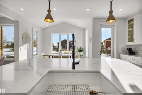 Kitchen featuring light stone countertops, pendant lighting, white cabinetry, glass fronted cabinets, and lofted ceiling - 11 Promenade Point(E), Beaumont, AB - Indoor Photo Showing Kitchen