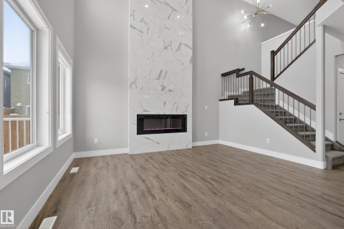 Unfurnished living room featuring a high ceiling, wood finished floors, a premium fireplace, and suspended lighting - 3224 160 Street, Edmonton, AB - Indoor With Fireplace