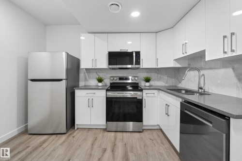 Kitchen with stainless steel appliances, dark stone countertops, light wood-type flooring, white cabinetry, and backsplash - 3224 160 Street, Edmonton, AB - Indoor Photo Showing Kitchen With Double Sink