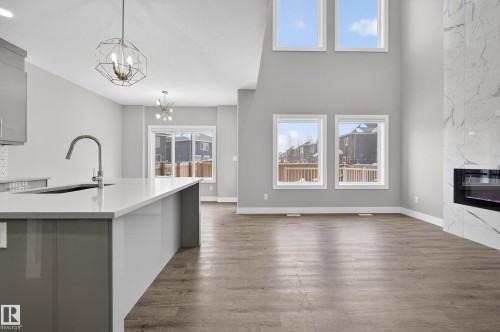 Kitchen with healthy amount of natural light, light stone counters, a premium fireplace, dark wood-type flooring, and a high ceiling - 3224 160 Street, Edmonton, AB - Indoor With Fireplace