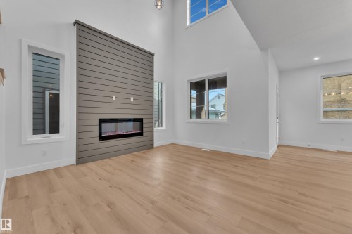 Unfurnished living room featuring a high ceiling, a glass covered fireplace, light wood-style flooring, and plenty of natural light - 6111 Crawford Drive, Edmonton, AB - Indoor Photo Showing Living Room With Fireplace