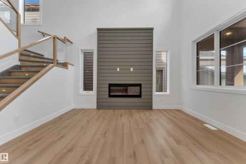 Unfurnished living room featuring plenty of natural light, a high ceiling, a glass covered fireplace, and light wood-type flooring - 6111 Crawford Drive, Edmonton, AB - Indoor With Fireplace