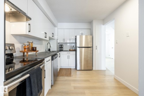 Kitchen featuring stainless steel appliances, dark countertops, white cabinets, light wood-style floors, and backsplash - 13449 40 Street, Edmonton, AB - Indoor Photo Showing Kitchen