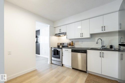 Kitchen featuring stainless steel appliances, light wood-style floors, white cabinetry, dark stone counters, and tasteful backsplash - 13449 40 Street, Edmonton, AB - Indoor Photo Showing Kitchen With Double Sink