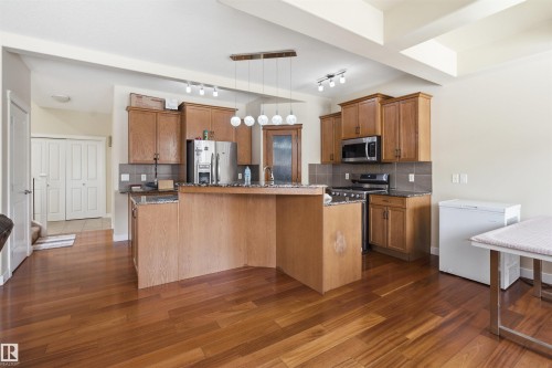 Kitchen with wood finish cabinetry, decorative backsplash, stainless steel appliances, dark wood-style floors, and rail lighting - 2923 16 Street, Edmonton, AB - Indoor Photo Showing Kitchen
