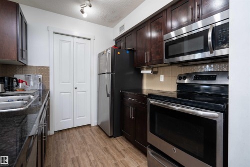 Kitchen featuring stainless steel appliances, a textured ceiling, backsplash, dark wood finish cabinets, and light wood-style floors - 415 111 Watt Common, Edmonton, AB - Indoor Photo Showing Kitchen With Double Sink