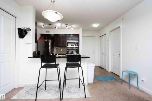 Kitchen with dark wood finish cabinets, backsplash, a peninsula, stainless steel appliances, and a kitchen bar - 415 111 Watt Common, Edmonton, AB - Indoor Photo Showing Kitchen