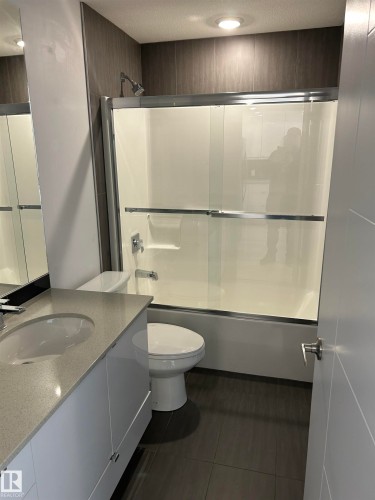 Bathroom with shower / bath combination with glass door, vanity, dark tile patterned floors, and a textured ceiling - 202 8510 90 Street, Edmonton, AB - Indoor Photo Showing Bathroom