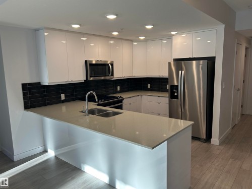 Kitchen with white cabinets, a peninsula, stainless steel appliances, light wood-type flooring, and modern cabinets - 202 8510 90 Street, Edmonton, AB - Indoor Photo Showing Kitchen With Double Sink With Upgraded Kitchen