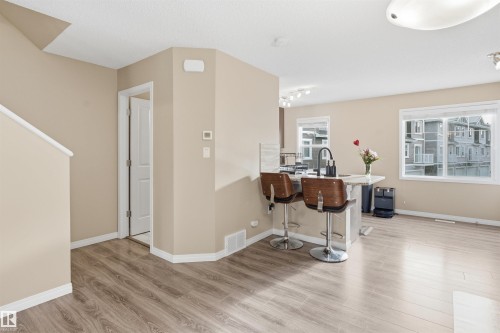 Kitchen with a breakfast bar, light wood-type flooring, a peninsula, and light stone counters - 48 1140 Chappelle Boulevard, Edmonton, AB - Indoor Photo Showing Other Room