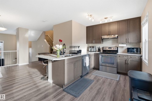 Kitchen featuring stainless steel appliances, light wood-style floors, a peninsula, a breakfast bar area, and dark wood finish cabinets - 48 1140 Chappelle Boulevard, Edmonton, AB - Indoor Photo Showing Kitchen With Stainless Steel Kitchen