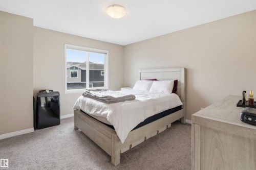 Bedroom with light colored carpet and black refrigerator - 48 1140 Chappelle Boulevard, Edmonton, AB - Indoor Photo Showing Bedroom