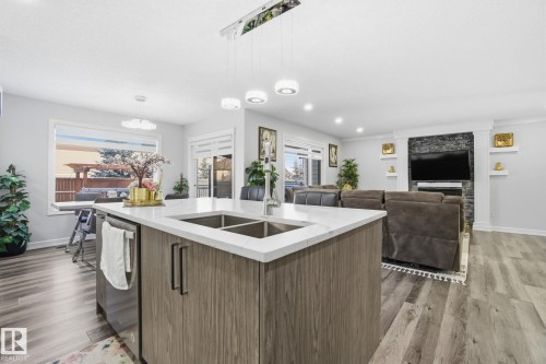 Kitchen featuring decorative light fixtures, light stone counters, dark wood-type flooring, a center island with sink, and recessed lighting - 1532 37C Avenue, Edmonton, AB - Indoor Photo Showing Kitchen With Double Sink