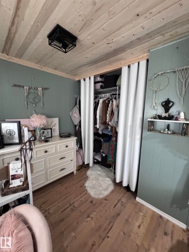 Bedroom with dark wood-style flooring, a closet, wood ceiling, and wooden walls - #44 9501 104 Ave, Westlock, AB - Indoor