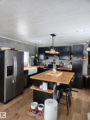 Kitchen with dark cabinetry, stainless steel appliances, a center island, decorative light fixtures, and light wood-style floors - #44 9501 104 Ave, Westlock, AB - Indoor