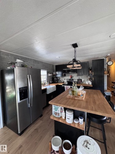Kitchen with dark cabinets, stainless steel appliances, a kitchen breakfast bar, wooden counters, and light wood-style floors - #44 9501 104 Ave, Westlock, AB - Indoor