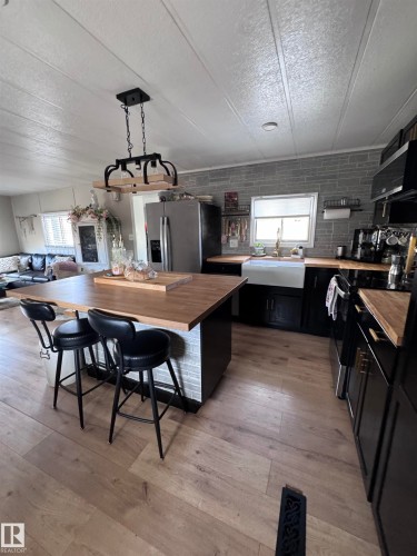 Kitchen featuring dark cabinetry, range with electric cooktop, butcher block countertops, a textured ceiling, and stainless steel refrigerator with ice dispenser - #44 9501 104 Ave, Westlock, AB - Indoor