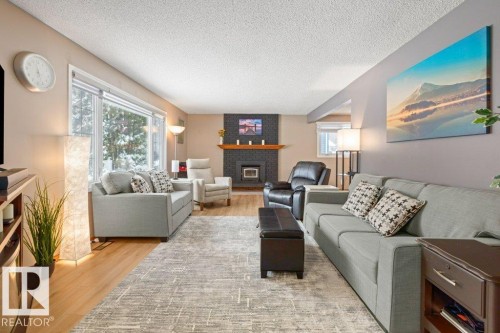 Living area with light wood-style floors, a textured ceiling, and a brick fireplace - 1 Larkspur Crescent, St. Albert, AB - Indoor Photo Showing Living Room With Fireplace