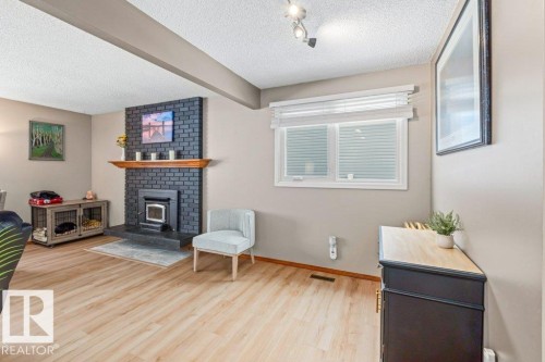 Sitting room featuring light wood-style floors, beamed ceiling, a textured ceiling, and a wood stove - 1 Larkspur Crescent, St. Albert, AB - Indoor With Fireplace