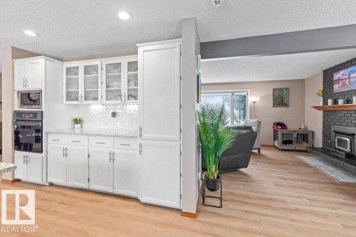 Kitchen with glass insert cabinets, white cabinets, oven, light wood finished floors, and a textured ceiling - 1 Larkspur Crescent, St. Albert, AB - Indoor With Fireplace