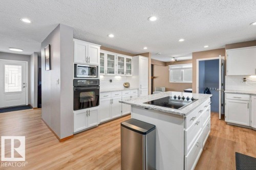 Kitchen with glass fronted cabinets, white cabinetry, black appliances, light stone counters, and light wood-style floors - 1 Larkspur Crescent, St. Albert, AB - Indoor Photo Showing Kitchen With Upgraded Kitchen