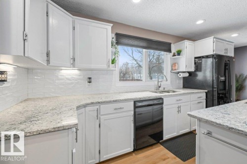 Kitchen with black appliances, light wood-style flooring, white cabinetry, light stone countertops, and a textured ceiling - 1 Larkspur Crescent, St. Albert, AB - Indoor Photo Showing Kitchen With Upgraded Kitchen