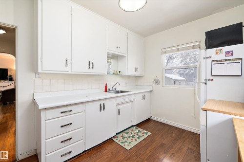 Kitchen with white cabinetry, tasteful backsplash, dark wood finished floors, and freestanding refrigerator - 11242 72 Avenue, Edmonton, AB - Indoor