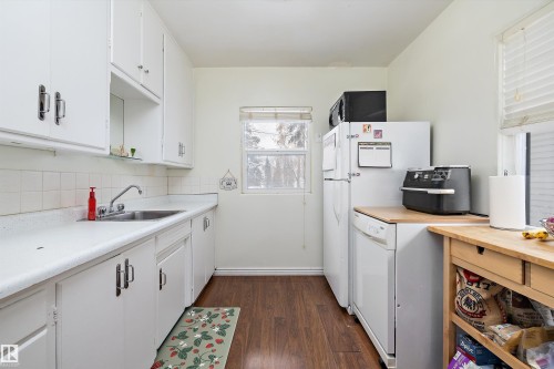 Kitchen featuring white cabinetry, light countertops, dark wood-style flooring, white appliances, and tasteful backsplash - 11242 72 Avenue, Edmonton, AB - Indoor Photo Showing Kitchen