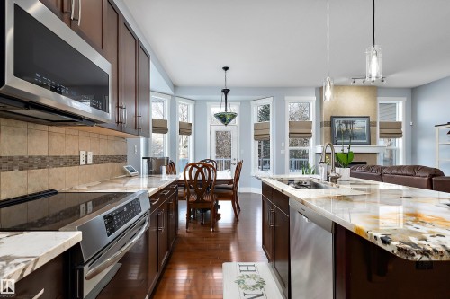 Kitchen with dark brown cabinets, stainless steel appliances, decorative light fixtures, light stone countertops, and dark wood-style flooring - 1409 Westerra Bay, Stony Plain, AB - Indoor Photo Showing Kitchen With Upgraded Kitchen