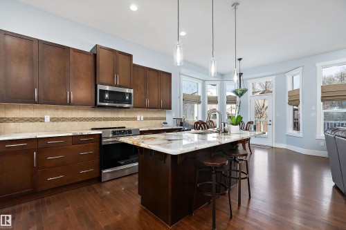 Kitchen with stainless steel appliances, a kitchen breakfast bar, dark brown cabinetry, pendant lighting, and light stone counters - 1409 Westerra Bay, Stony Plain, AB - Indoor Photo Showing Kitchen With Upgraded Kitchen