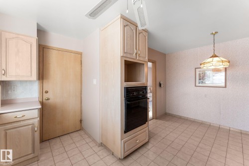 Kitchen featuring light wood finish cabinetry, wallpapered walls, black oven, light countertops, and pendant lighting - 3519 111B Street, Edmonton, AB - Indoor Photo Showing Kitchen