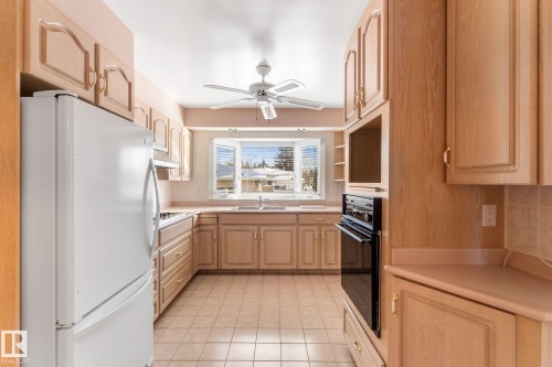 Kitchen with freestanding refrigerator, light wood finish cabinetry, light countertops, oven, and a ceiling fan - 3519 111B Street, Edmonton, AB - Indoor Photo Showing Kitchen With Double Sink