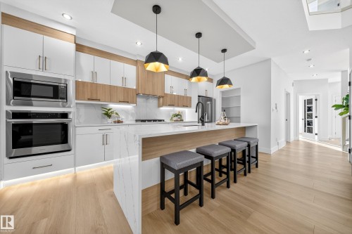 Dual tone kitchen with stainless steel appliances, a breakfast bar, decorative light fixtures, light wood-type flooring, and light stone counters - 9907 68 Street, Edmonton, AB - Indoor Photo Showing Kitchen With Upgraded Kitchen