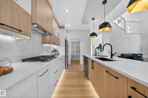 Two tone kitchen with dual tone cabinets, modern cabinets, light stone counters, pendant lighting, and light wood-style flooring - 9907 68 Street, Edmonton, AB - Indoor Photo Showing Kitchen With Double Sink With Upgraded Kitchen