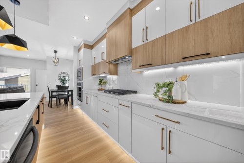 Kitchen featuring dual tone cabinetry, pendant lighting, light stone countertops, light wood-style flooring, and stainless steel appliances - 9907 68 Street, Edmonton, AB - Indoor Photo Showing Kitchen With Upgraded Kitchen