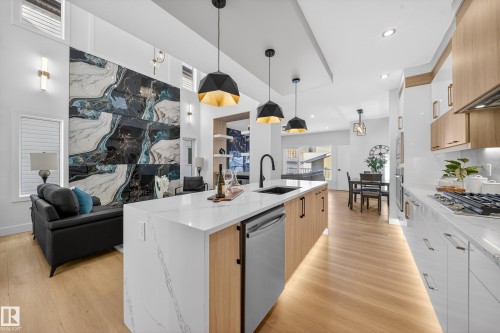 Two tone kitchen featuring open floor plan, dual tone cabinets, pendant lighting, light stone counters, and modern cabinets - 9907 68 Street, Edmonton, AB - Indoor Photo Showing Kitchen With Upgraded Kitchen