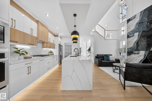 Kitchen with two tone cabinetry, open floor plan, decorative light fixtures, stainless steel appliances, and light wood finished floors - 9907 68 Street, Edmonton, AB - Indoor Photo Showing Kitchen With Upgraded Kitchen