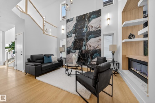 Living area with a glass covered fireplace, a high ceiling, and light wood finished floors - 9907 68 Street, Edmonton, AB - Indoor Photo Showing Living Room With Fireplace