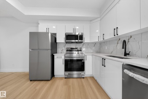 Kitchen with stainless steel appliances, tasteful backsplash, light wood finished floors, white cabinetry, and light stone counters - 9907 68 Street, Edmonton, AB - Indoor Photo Showing Kitchen