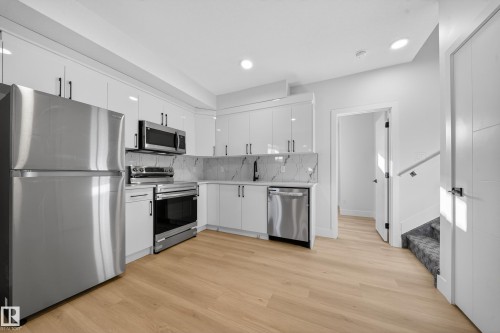Kitchen with stainless steel appliances, white cabinetry, light wood-style floors, backsplash, and recessed lighting - 9907 68 Street, Edmonton, AB - Indoor Photo Showing Kitchen
