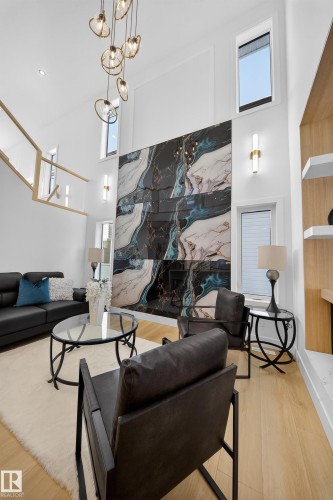 Living area featuring a high ceiling, light wood-type flooring, a high end fireplace, and a chandelier - 9907 68 Street, Edmonton, AB - Indoor